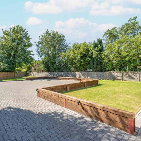 Secure parking area. The space is paved, bordered by a low timber wall separating it from the lawn area.