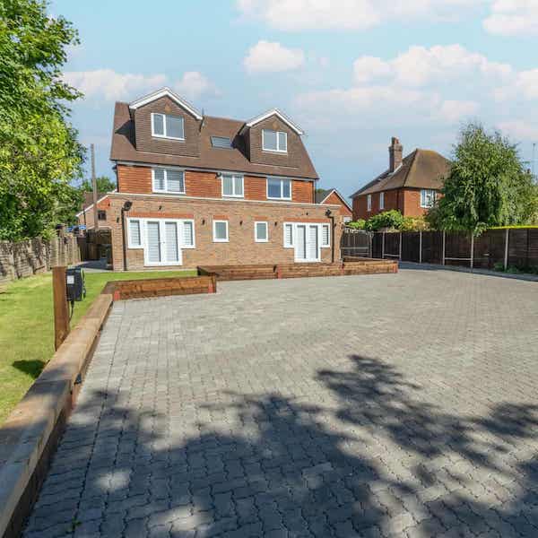 Rear view of the building across the parking area. Electric car charging point on the left of the image. The ground floor apartments have patio doors leading directly to the lawn.