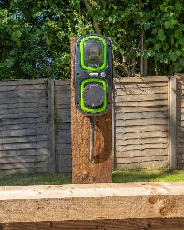 An electric car charging point mounted on a stake above the low timber wall on the edge of the car park.