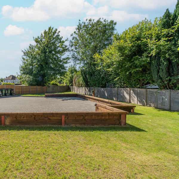 Lawn in the foreground leading to a low timber wall and the parking area. The lawn runs down the right hand side to the far end of the garden