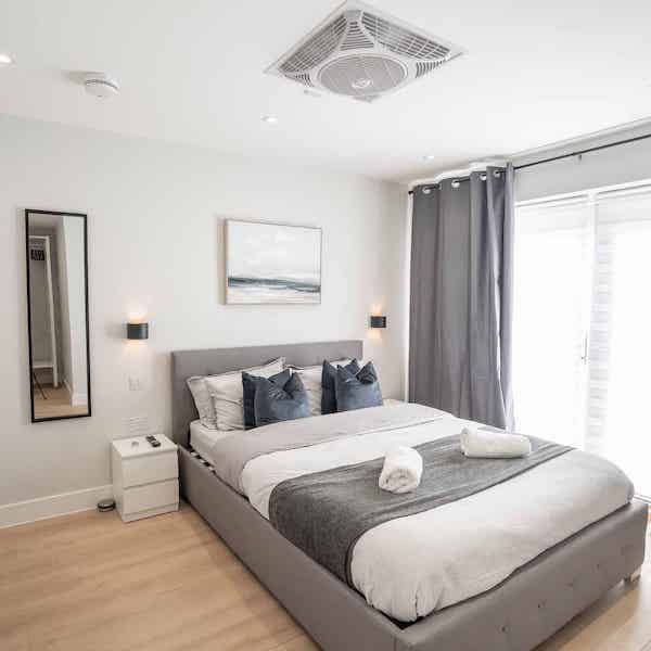 A double bed next to a french window, with coastal painting above the bed and a tall mirror on the left of the image.
