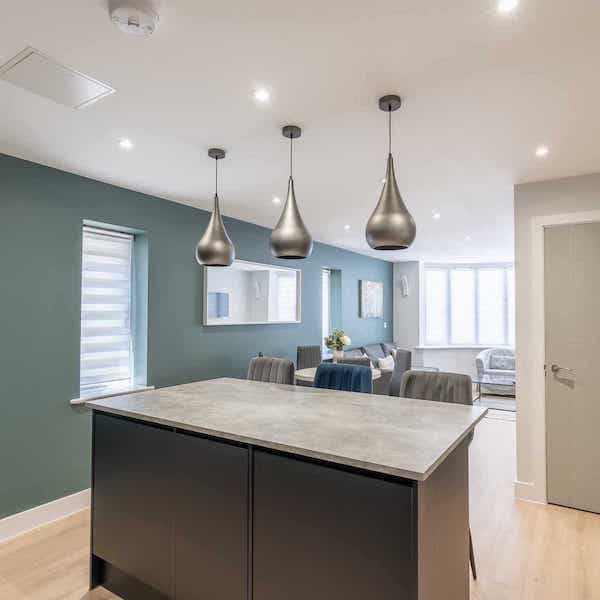 A view of the breakfast bar with three bar stools behind, and the living space beyond, with the bay window at the end of the room.
