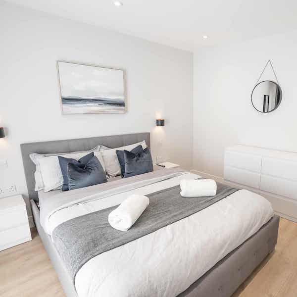 An example bedroom with double bed made with four pillows and four cushions. There is also a wooden floor and storage on either side of the bed.